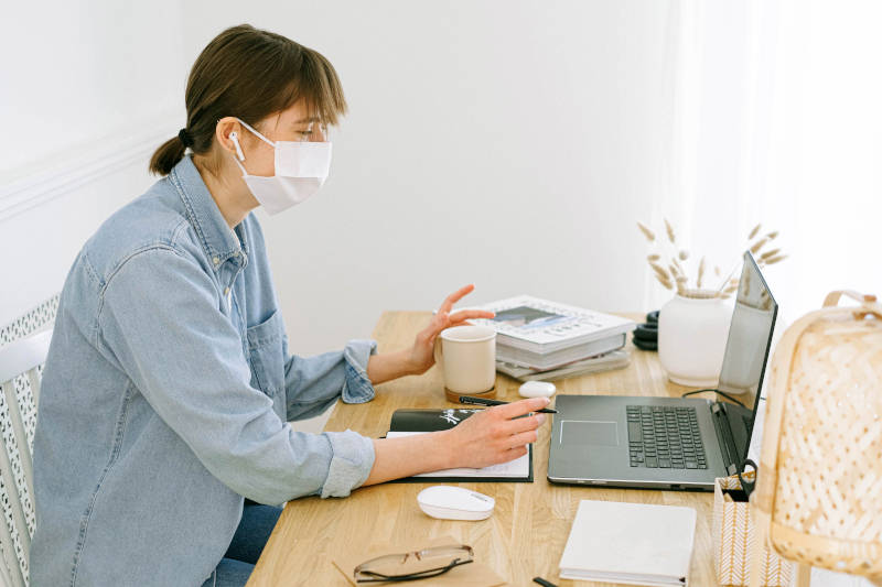 Une jeune femme avec un masque chirurgical devant son ordinateur pour publier du contenu sur son blog
